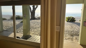 A beach view from a room with a window, a chair, and a door leading to the beach.