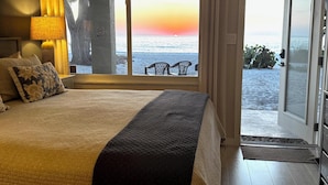 A bedroom with a large bed, a view of the beach, and a sliding glass door leading outside.