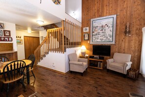 A wooden-floored living room with a staircase, a television, and a framed map on the wall.