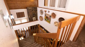 Eine Holztreppe mit Handlauf, eine Steinwand und verschiedene Wanddekorationen, darunter ein gerahmtes Bild und gewebte Körbe.