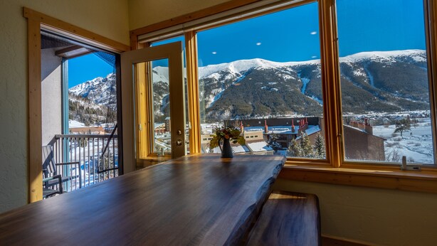 Un tavolo in legno con vista su montagne innevate e un cielo sereno visibile attraverso ampie finestre.