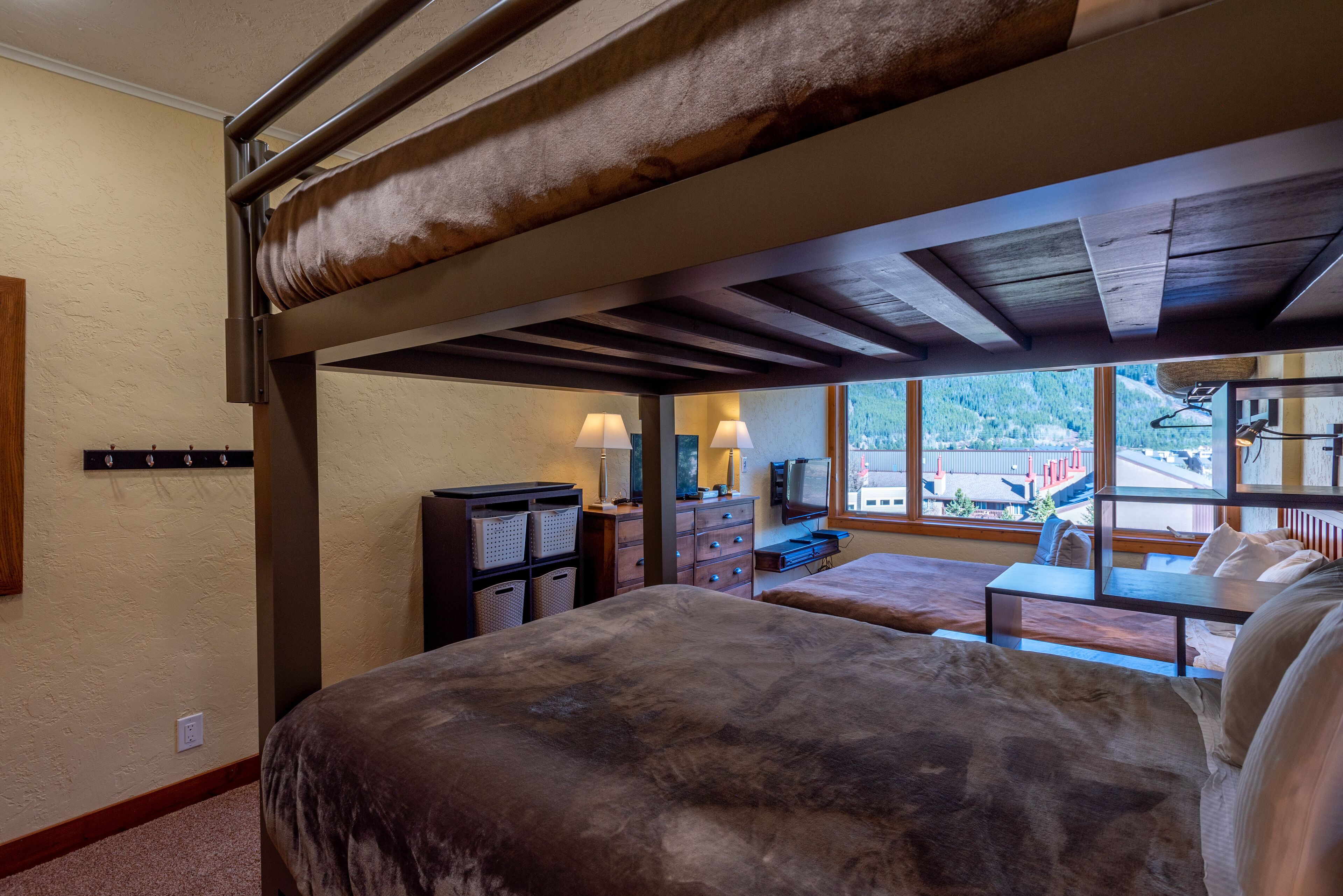 A bedroom with a bunk bed, a desk, and a view of a mountain.