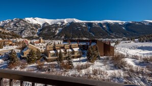 Paesaggio montano innevato con un complesso turistico che include diversi edifici, tra cui un grande lodge con tetto spiovente e una più piccola baita.