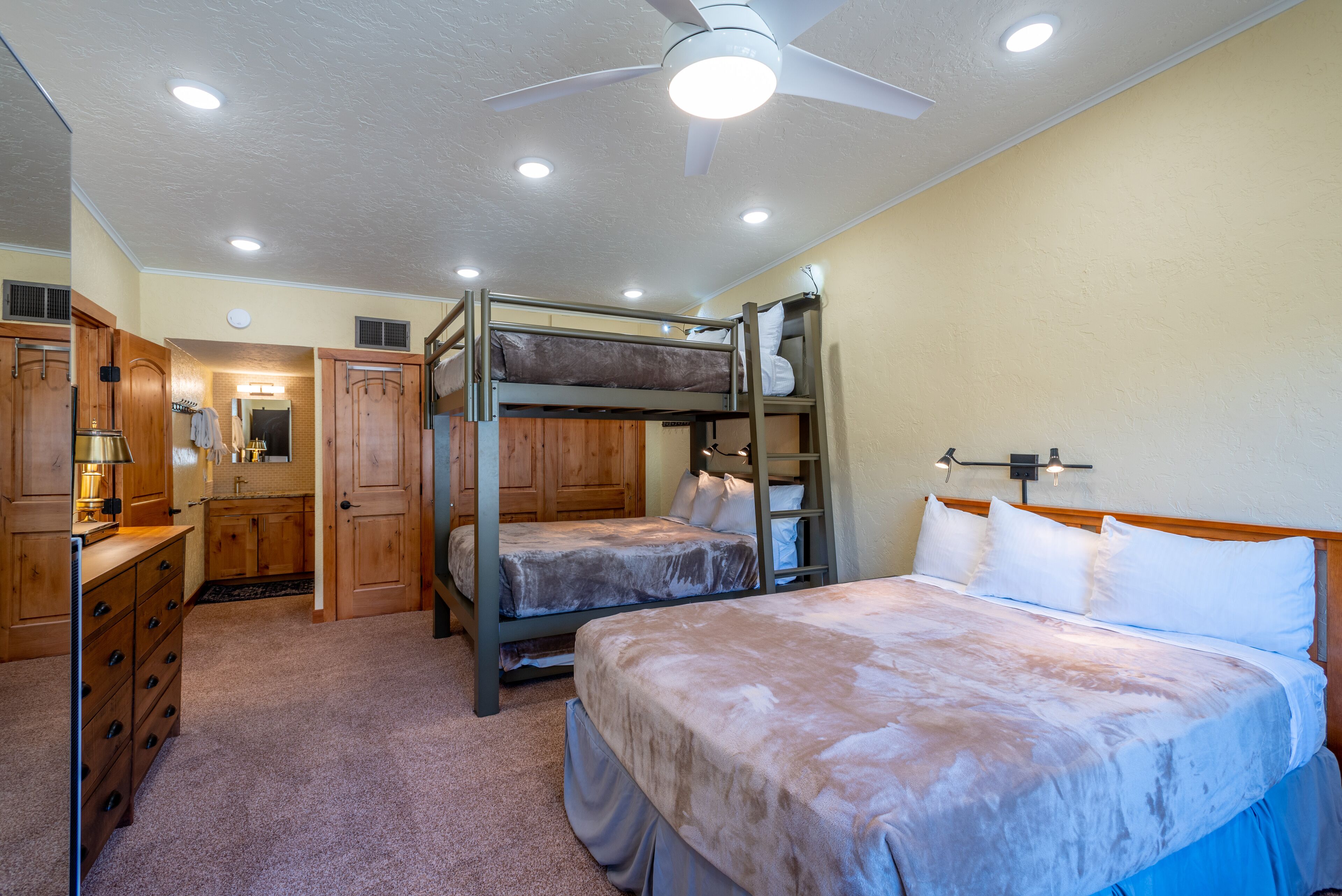 A room with bunk beds, a dresser, and a ceiling fan.