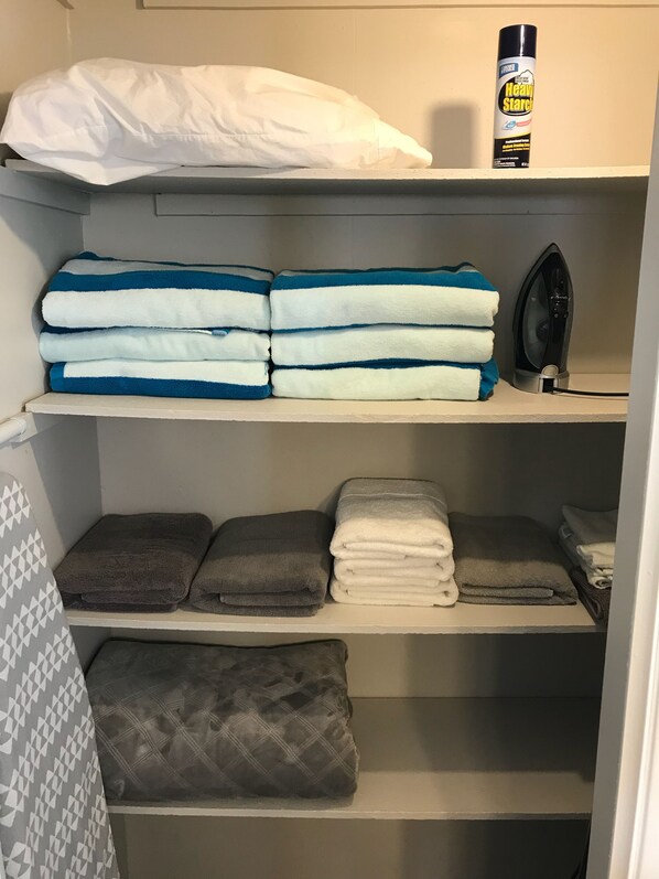 A neatly organized storage area with folded towels in blue and white, a white pillow, a can of heavy starch, and an iron.