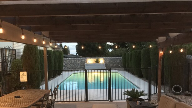 Un patio al aire libre con piscina, mobiliario y luces colgantes.