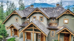 Una casa de madera de varios pisos con techo a dos aguas, varias entradas y un paisaje montañoso de fondo.