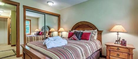 Un dormitorio con una cama grande, una mesita de noche de madera, un espejo y una lámpara.
