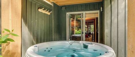 Un jacuzzi en un área exterior de madera con una puerta que da a un porche cubierto.