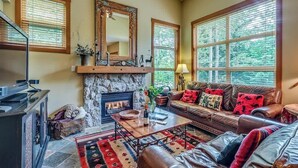 Una sala acogedora con chimenea, sofá de cuero y ventanas amplias.