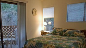 A bedroom with a bed, a nightstand, a window with blinds, a clock on the wall, and a view of the outdoors through a sliding door. - A01: 2 Bedroom, 2.5 Bath, Townhouse Style Condo (Avalon)