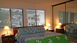 A bedroom with a bed, two bedside tables, a nightstand, a mirror, and a window with blinds. - A01: 2 Bedroom, 2.5 Bath, Townhouse Style Condo (Avalon)