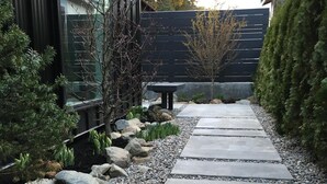 A pathway lined with rocks and small plants, leading to a building with a dark facade and a glass window.