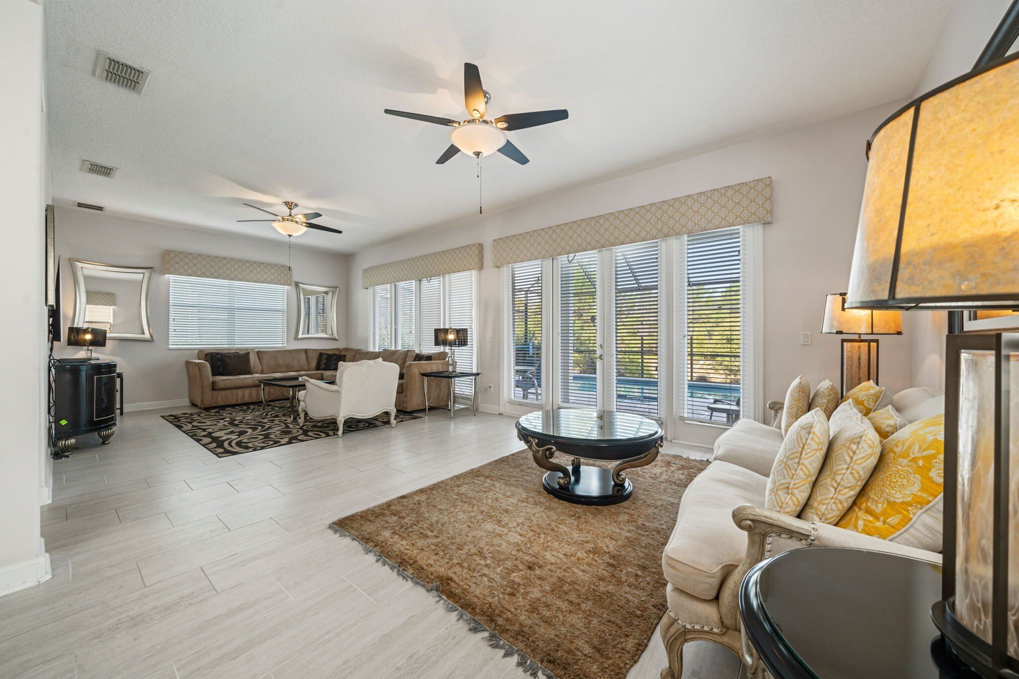 A spacious living room with a high ceiling, ceiling fans, a large round coffee table, and a seating area with a sofa and armchairs.