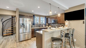 A modern kitchen with a central island, stainless steel appliances, and a staircase leading to another level.