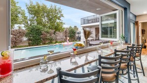A bar area with a pool view, outdoor seating, and a dining table with chairs.