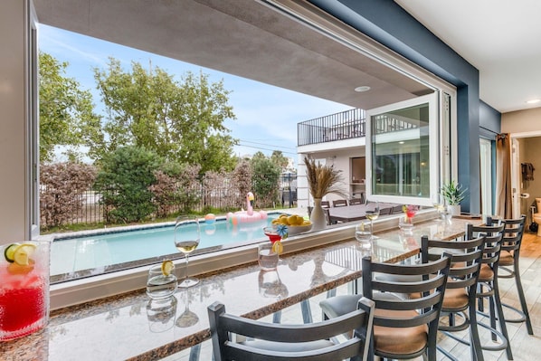 A bar area with a pool view, outdoor seating, and a dining table with chairs.