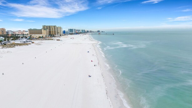 A wide sandy beach with a clear view of the ocean and a city skyline in the background.