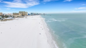 A wide beach with a pier extending into calm waters, surrounded by high-rise buildings.
