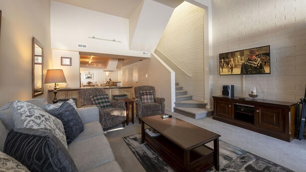 A spacious living room with a sofa, armchairs, a coffee table, and a TV mounted on the wall. A staircase leads to an upper level. - Sunlit Park City 3BR+Loft Sleeps 8, In-Unit Laundry-Walk to Park City Resort (Park City)
