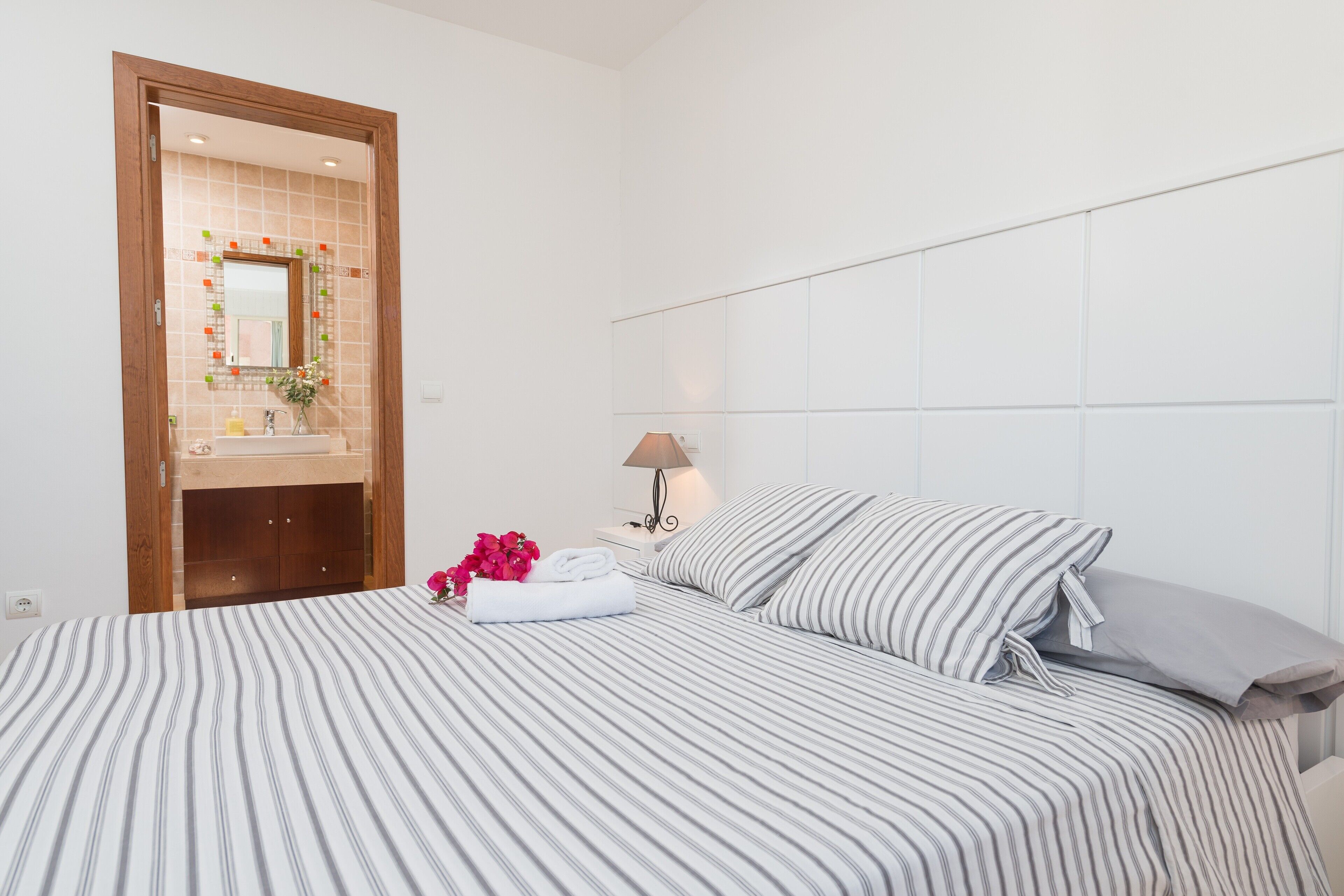 Une chambre d’hôtel avec un lit, une table de chevet, une lampe, une salle de bain avec un miroir et une porte en bois.