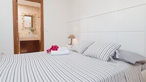 Una habitación de hotel con cama, mesita de noche, lámpara, baño con espejo y puerta de madera.