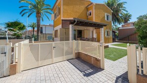 Un edificio residencial de dos plantas con fachada amarilla, un acceso con portón y un patio pavimentado.