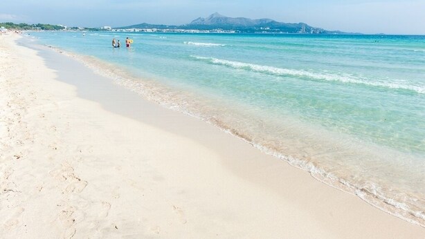 Una playa con agua turquesa cristalina, una orilla de arena y una montaña al fondo.