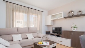 Una sala de estar moderna con un sofá color beige, una mesa de centro con una bandeja de limones y vasos, un televisor de pantalla plana y un aparador con platos decorativos.