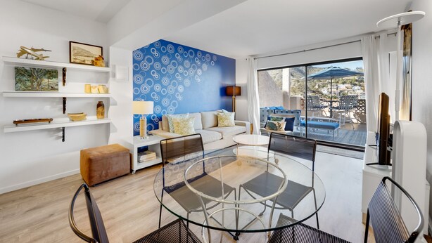 A modern living room with a blue patterned wall, a sofa, a coffee table, and a balcony with outdoor furniture.
