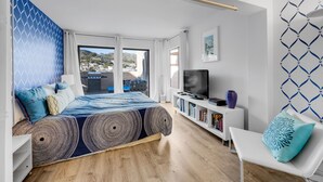 A modern bedroom with a large bed, a TV, and a bookshelf.