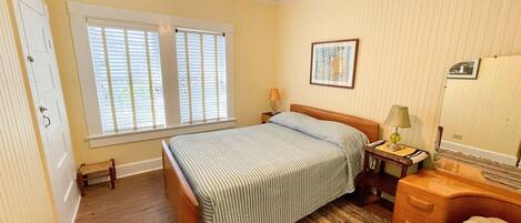 Un dormitorio con cama, mesita de noche, cómoda, ventilador de techo y ventana con persianas.