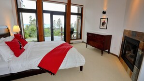 A bedroom with a large bed, a fireplace, a view of the outdoors, and a wooden dresser.