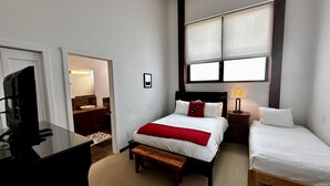 A hotel room with a bed, a bedside table with a lamp, a TV, and a bathroom visible through an open door.