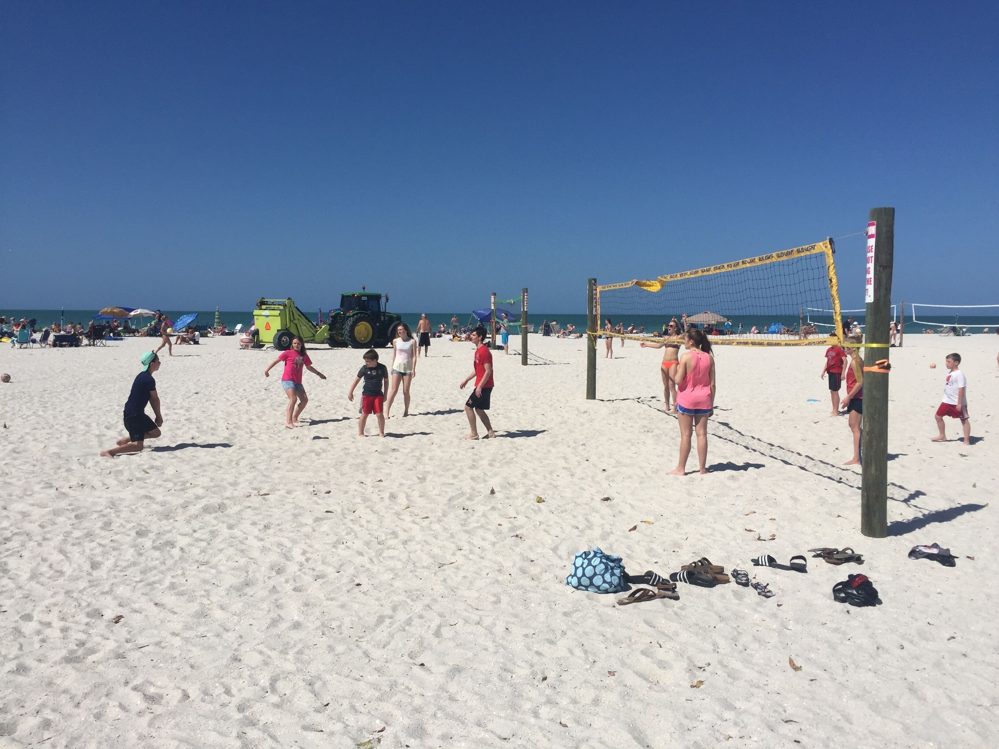A beach volleyball game with players and spectators.