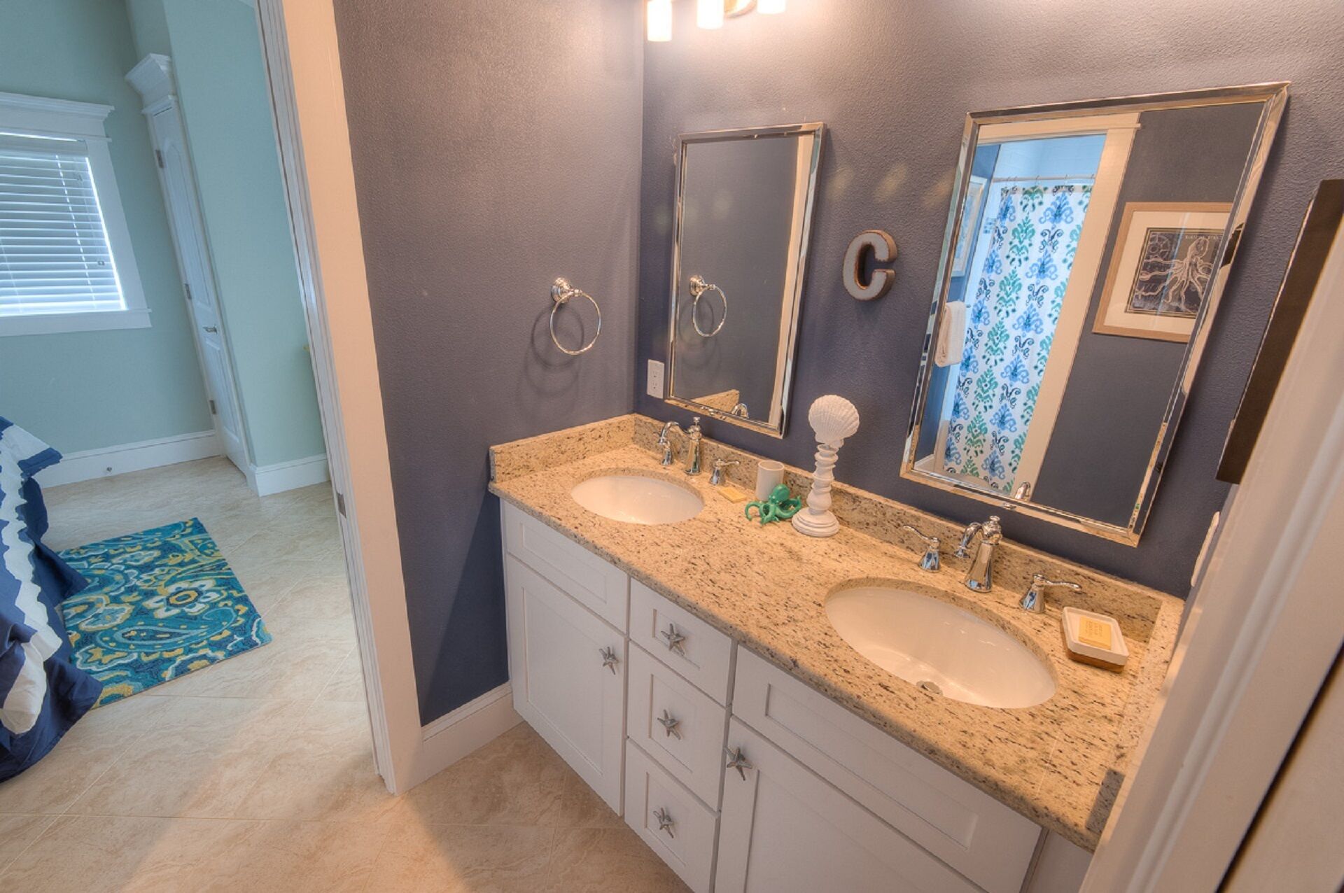 A bathroom with two sinks, a mirror, and a towel rack. There is a patterned rug on the floor.