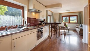 Une cuisine moderne dotée d’un îlot central, d’un coin repas avec une table et des chaises, et offrant une vue sur l’extérieur grâce à de grandes fenêtres.