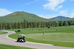 A golf course with a paved driving range, a clubhouse, and a scenic mountainous backdrop.