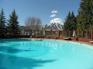 A clear blue pool with a mountain view, surrounded by trees and a wooden deck.