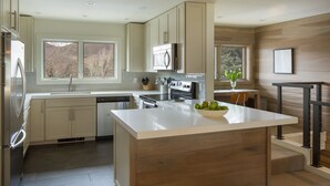 Une cuisine moderne dotée d’un îlot central, d’appareils électroménagers en acier inoxydable et de meubles de rangement en bois.