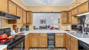 Cocina compacta con armarios de madera, horno empotrado, lavavajillas y una isla central con fregadero.