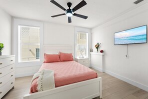 Ein Schlafzimmer mit einem Bett, einem Deckenventilator, einem Fernseher und einem Fenster mit Jalousien.