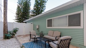 Un patio con un tapete azul estampado, muebles de exterior color beige y una casa verde.