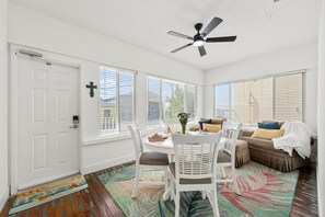 Habitación luminosa y bien iluminada, con ventilador de techo, una mesa de comedor con sillas, un sofá y una ventana con persianas.