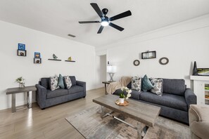 Ein modernes Wohnzimmer mit zwei grauen Sofas, einem Holztisch und einem Deckenventilator.