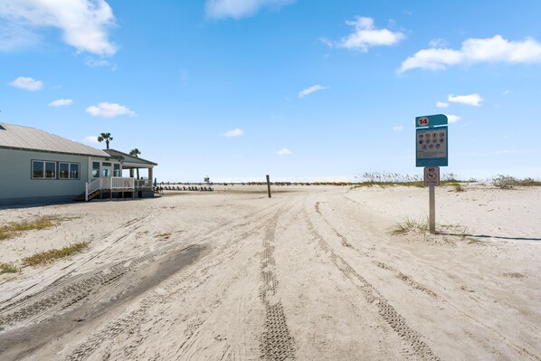 A beach with a building on the left, a signpost with a '14' and 'ALCOHOL' prohibition, and a clear sky.