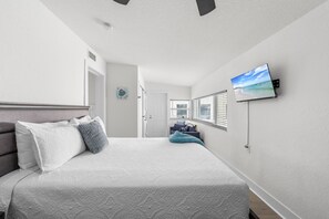 A bedroom with a bed, a television mounted on the wall, and a door leading to another room.