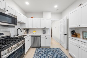 A modern kitchen with white cabinetry, stainless steel appliances, and a blue patterned rug. - Bright Beach Cottage w/ Patio l Steps to the Beach & Restaurants l Pet-Friendly (Clearwater)