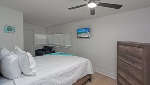 Un dormitorio con cama, cómoda, ventilador de techo y ventana con persianas.