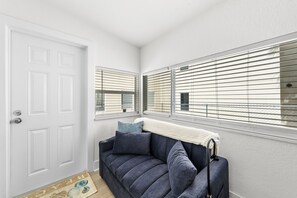Una habitación con una puerta blanca, una ventana con persianas, un sofá con una manta y un felpudo con diseño de pez.